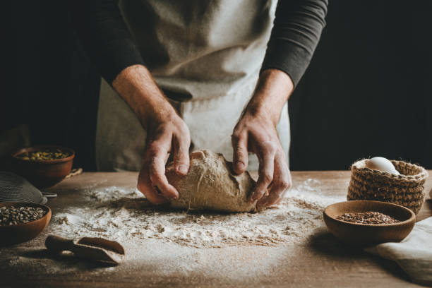 istock Young man kneading dough on dark background. 1404874907