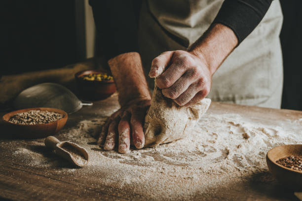 istock Young man kneading dough on dark background. 1404874976