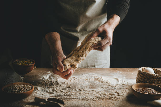 istock Young man kneading dough on dark background. 1404874977