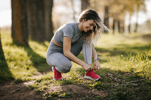 Young woman tying shoelace while preparing for jogging in nature