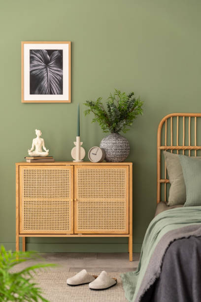 istock Stylish composition of modern bedroom interior. Mock up poster frame, rattan commode, beautiful bedclothes and creative personal accessories. Sgae green wall. Template. Copy space. 1404879926