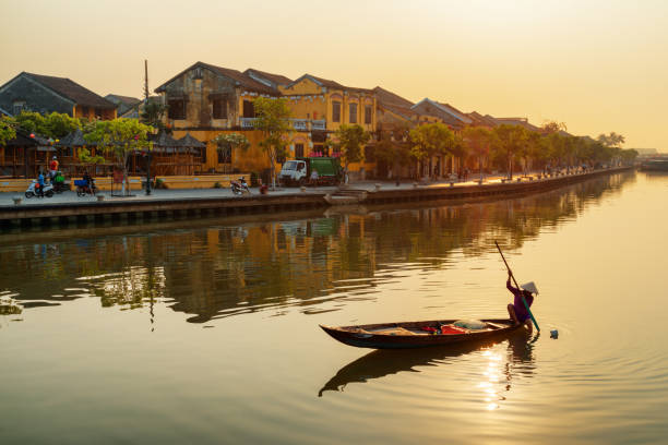 Awesome view of Vietnamese woman on boat at sunrise, Hoian Vietnamese woman in traditional bamboo hat on wooden boat rowing on the Thu Bon River at Hoi An Ancient Town at sunrise in Vietnam. Hoian is a popular tourist destination of Asia. hoi an stock pictures, royalty-free photos & images