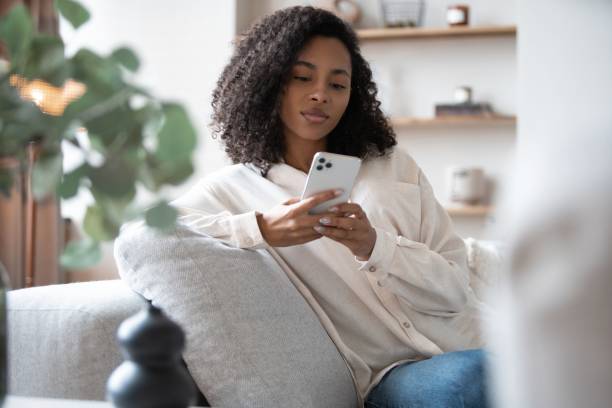 istock Smiling young mixed race woman sit on sofa at home using cellphone texting chatting with friend 1404882155