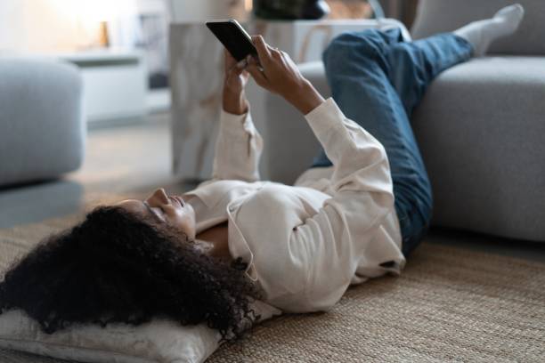 istock Young mixed race woman lying on floor at home using cellphone texting chatting with friend 1404882204
