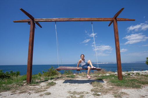 Happy child girl on swing in summer day, travel, vacation and holidays concept