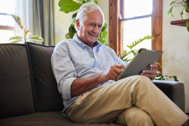 istock Smiling senior man sitting on a sofa at home and using a tablet 1404883595