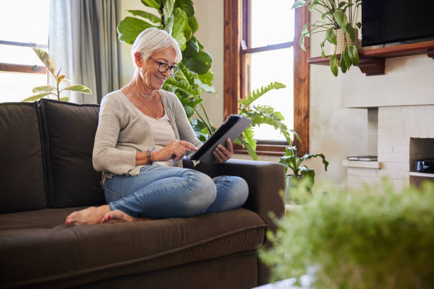 istock Smiling senior woman using a digital tablet on a sofa at home 1404883970