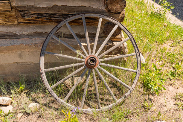 Old Wagon Wheel against Cabin Wall Old weathered wagon wheel leaning against a log cabin wall rusty old wagon detail stock pictures, royalty-free photos & images