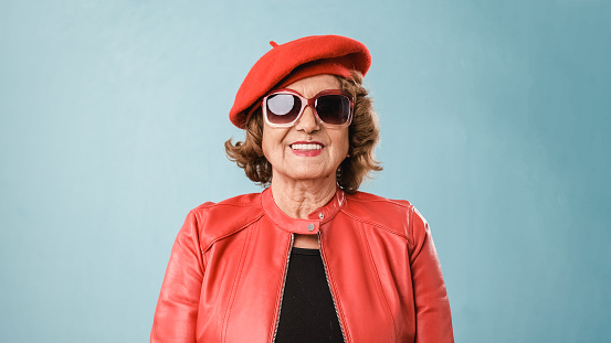 Modern and fashion older woman looking to camera dressed in red, on blue background