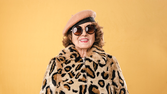 Stylish senior woman in sunglasses wearing an animal print coat and a beret while posing over an isolated background.