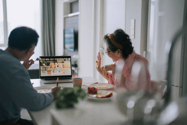 patrząc przez ramię azjatycka chińska para seniorów wideownuczka przy użyciu laptopa w jadalni podczas weekendowego porannego śniadania w wolnym czasie - grandparent using computer laptop dining table zdjęcia i obrazy z banku zdjęć