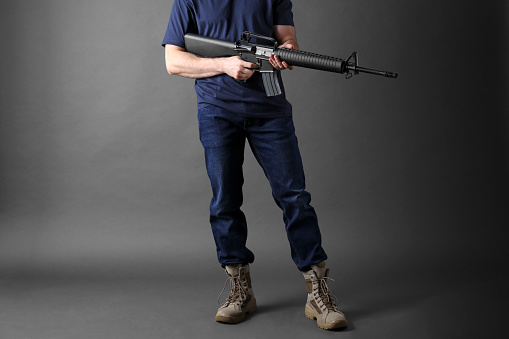 Assault gun. Man holding rifle on dark background, closeup