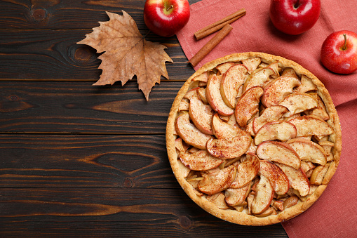 Delicious apple pie, fresh fruits and cinnamon on wooden table, flat lay. Space for text