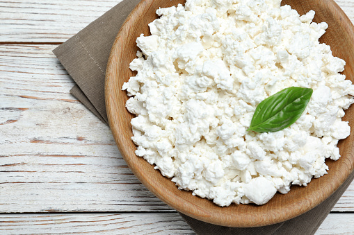 Delicious cottage cheese with basil on white wooden table, top view