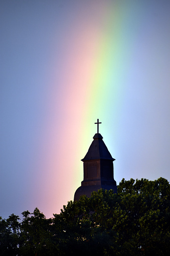 Rainbow on church tower with trees in the foreground