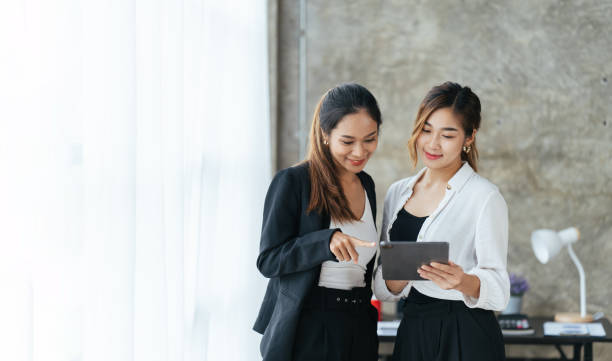 istock Smiling businesswoman talking with partner while standing in modern office interior, team of professional employees discussing ideas of project after working on touch pad. 1404892533