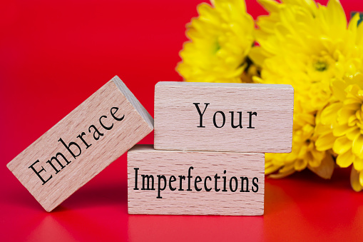 Embrace your imperfections text on wooden cube and with flowers bouquet background.