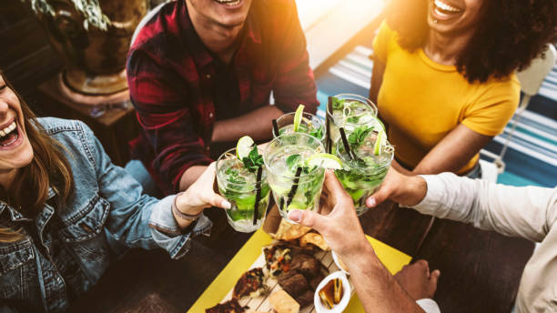 バーレストランでモヒートを応援する多人種の友人 - トロピカルカクテルパブで飲み物を乾杯し、前菜を食べるハッピーアワーを祝う若者 - 飲み物と若者のライフスタイルコンセプト - mojito ストックフォトと画像
