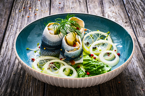 Marinated herring fillets with pickled cucumber, dill and onion on wooden table