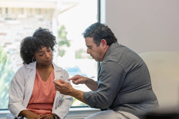 istock Male patient points to pill bottle while talking to doctor 1404901945