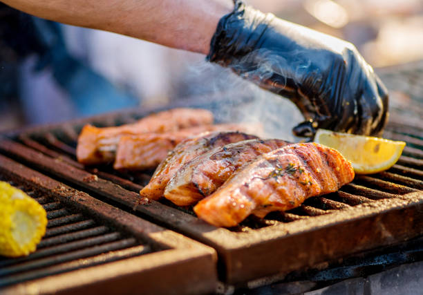 Cooking BBQ Fish. Gloved hands turn pieces of fish on the grill. Grilled salmon on a charcoal grill. Picnic in the backyard during a family holiday. stock photo