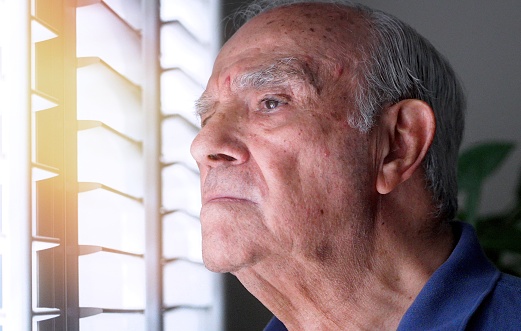 Serious, worried, stressed mature man looking through a window