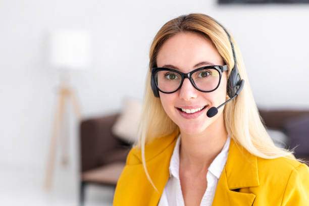 Portrait of young woman customer support call center operator or receptionist in headset at workplace, help service and client consulting call center concept, looking at the camera and smiling stock photo