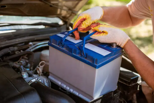 A man removes a battery from under the hood of a car. Battery replacement and repair.