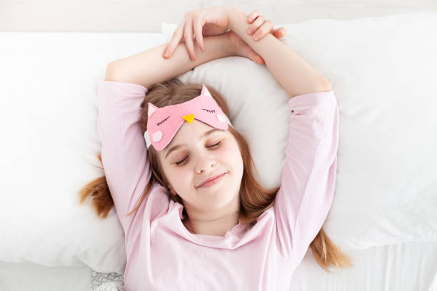 Cute girl wearing funny sleeping mask enjoying morning in a bed awaking up. stock photo