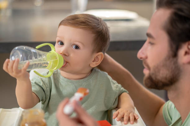 istock Cute little boy drinking from his bottle while dad feeding him 1404906546
