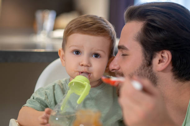 istock Cute little boy drinking from his bottle while dad feeding him 1404906552