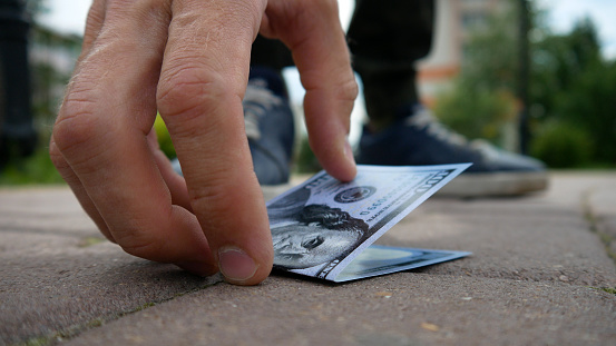 A walking man finds a hundred dollar bill on the sidewalk