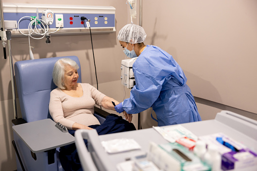 Nurse preparing a senior cancer patient for her chemotherapy at the hospital â medical treatment concepts