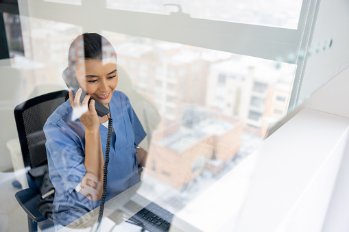 Latin American woman working as a receptionist at the hospital and talking on the phone - healthcare and medicine concepts