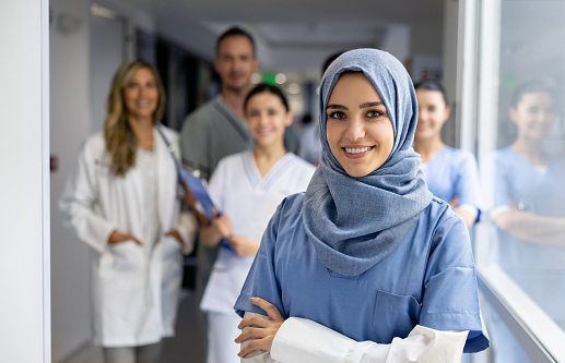 Portrait of a happy Muslim nurse working at the hospital and smiling in front of a group of healthcare workers