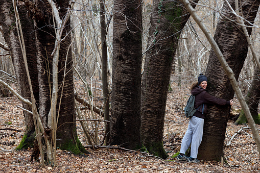 People and nature. Mid adult woman going for a walk in the forest. Hugging an old oak tree.