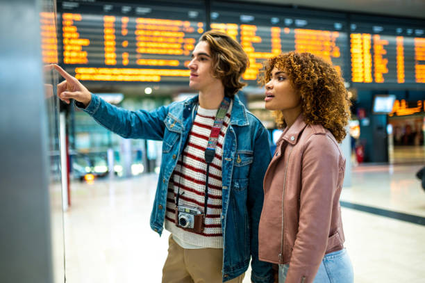 Youn couple buying ticket at the ticket machine Young couple searching for information about the departure of train. They are buying the ticket on the ticket machine tourist couple candid travel stock pictures, royalty-free photos & images