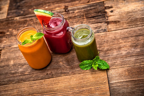 Three colorful fruit smoothie drinks in retro glass jar bottles on a old wooden background
