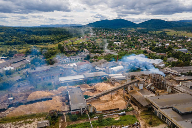 vista aérea da fábrica de processamento de madeira com pilha de fumaça do ambiente poluente do processo de produção no pátio de fabricação da fábrica - rasto de fumo de avião - fotografias e filmes do acervo