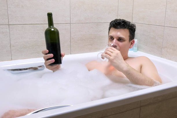 istock Tired drunk man lies in bath, pour and drinks wine from a wine glass. 1404923529