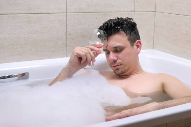 istock Drunk man is drinking red wine and falling asleep in bath. 1404923531