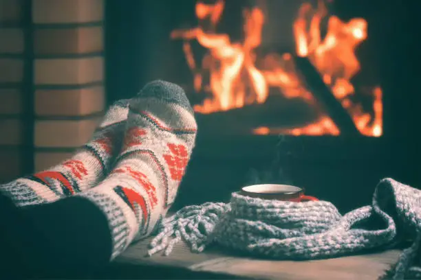 Girl resting and warming her feet by a burning fireplace in a country house on a winter evening. Selective focus
