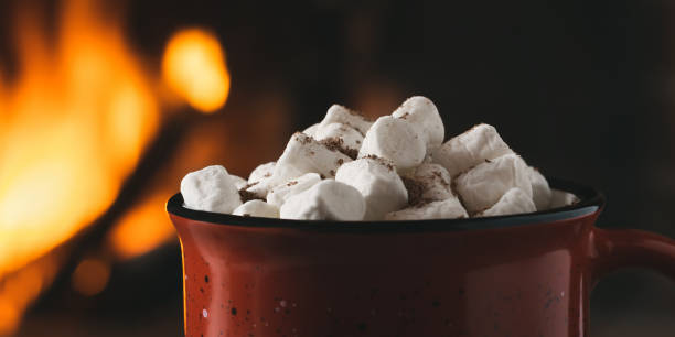 istock Cocoa with marshmallows and chocolate in a red mug near a burning fireplace, horizontal banner 1404925533