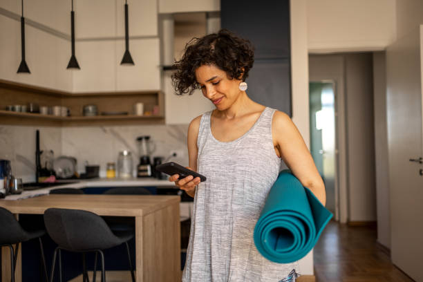 Woman getting ready for her yoga practice Woman getting ready for yoga practice, she is using her mobile phone to find suitable music 40 44 years stock pictures, royalty-free photos & images