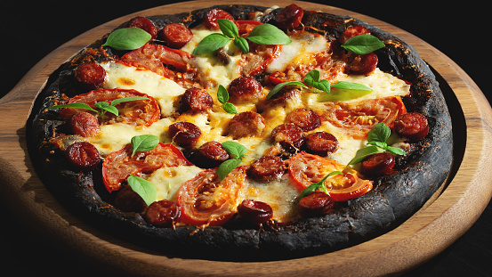 Black pizza with tomatoes, sausages, mozzarella and basil. Dough with healthy bamboo charcoal powder.