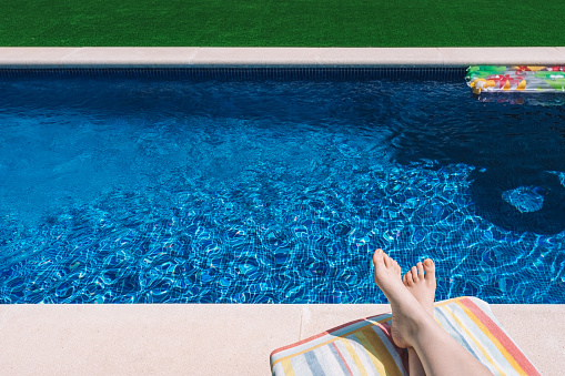 view of the feet of a young woman lying in a hammock by a swimming pool. woman enjoying a summer holiday in a hotel. concept of travel and leisure. natural sunlight, outside, garden with swimming pool.
