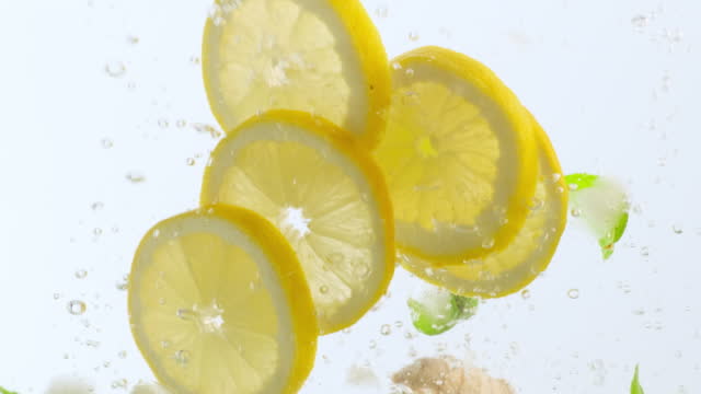 Lemon, mint and ginger floating in water. Fresh yellow lemons falling into water with bubbles on white background. Citrus fruits falling in water with bubbles slow motion close-up