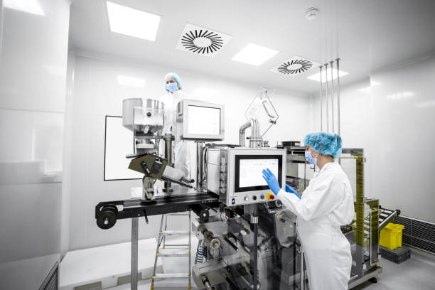Woman in a laboratory wearing protective gloves, mask, cap and suit seen in front of the screen on the machine in a pharmaceutical factory stock photo