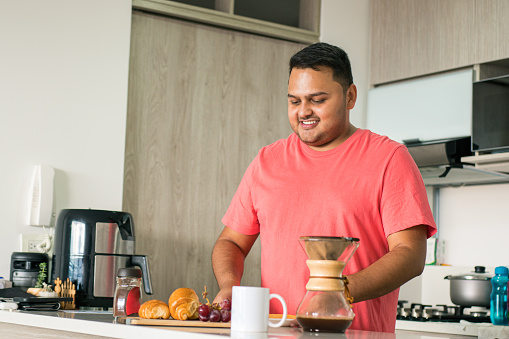 Lifestyle: Man dieting to lose weight and have better health. Latin American young adult in the kitchen of his house preparing a healthy breakfast.  correct problems of obesity and sedentary lifestyle