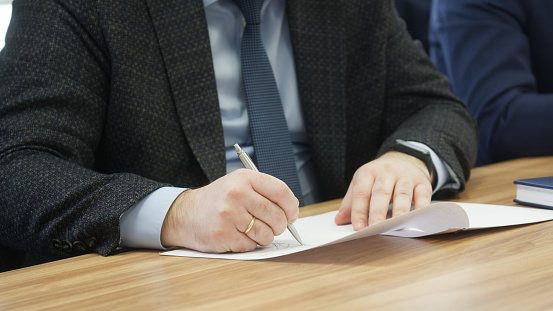 Politician or a businessman signs a memorandum, contract or agreement. Participation in meetings, negotiations and signing documents. No face. Close-up